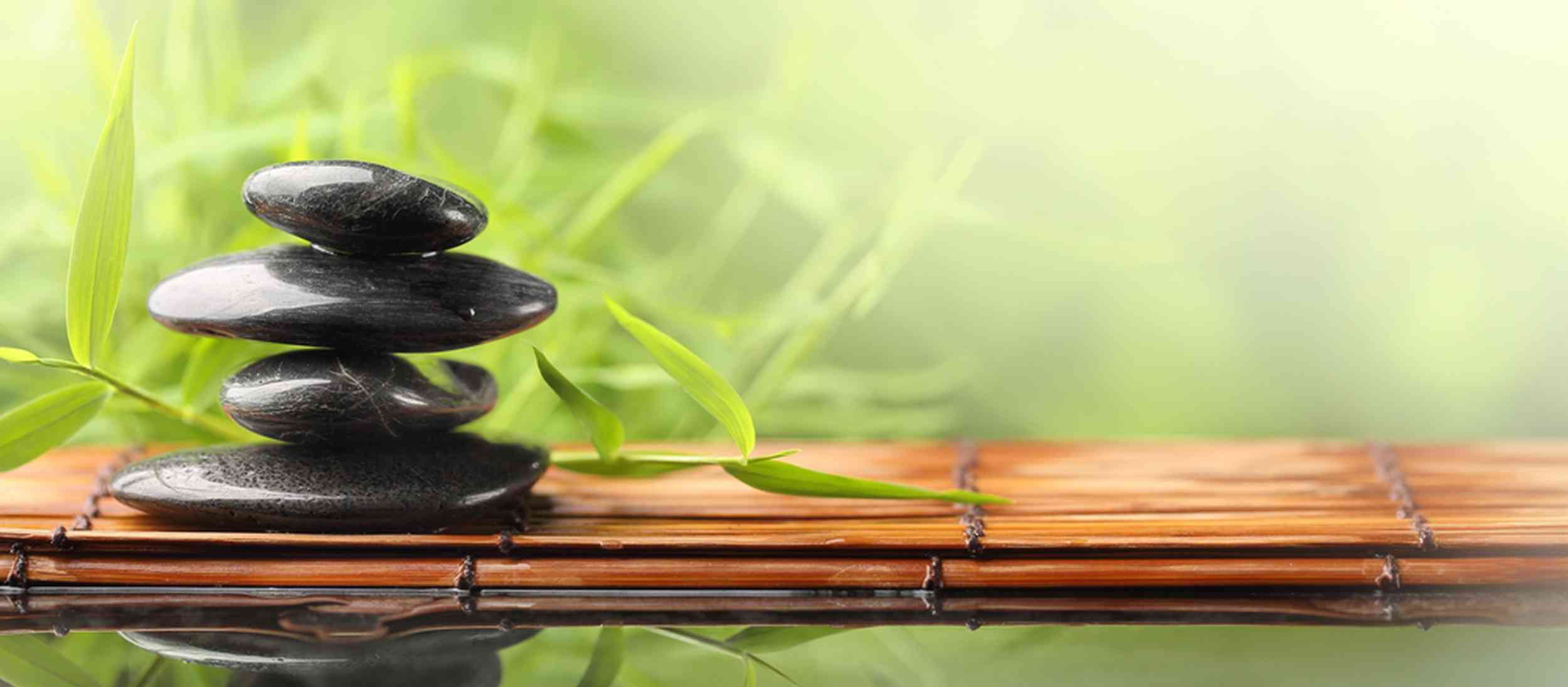 Pyramide_de_pierres_noires_sur_des_bambous_séchés_horizontaux_posés_sur_l_eau_bambous_verts_en_arrière_plan